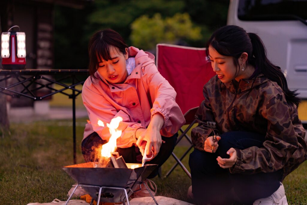 夜のオートキャンプ場で焚き火台を囲んで薪をくべる2人の女性と女子キャンプの様子