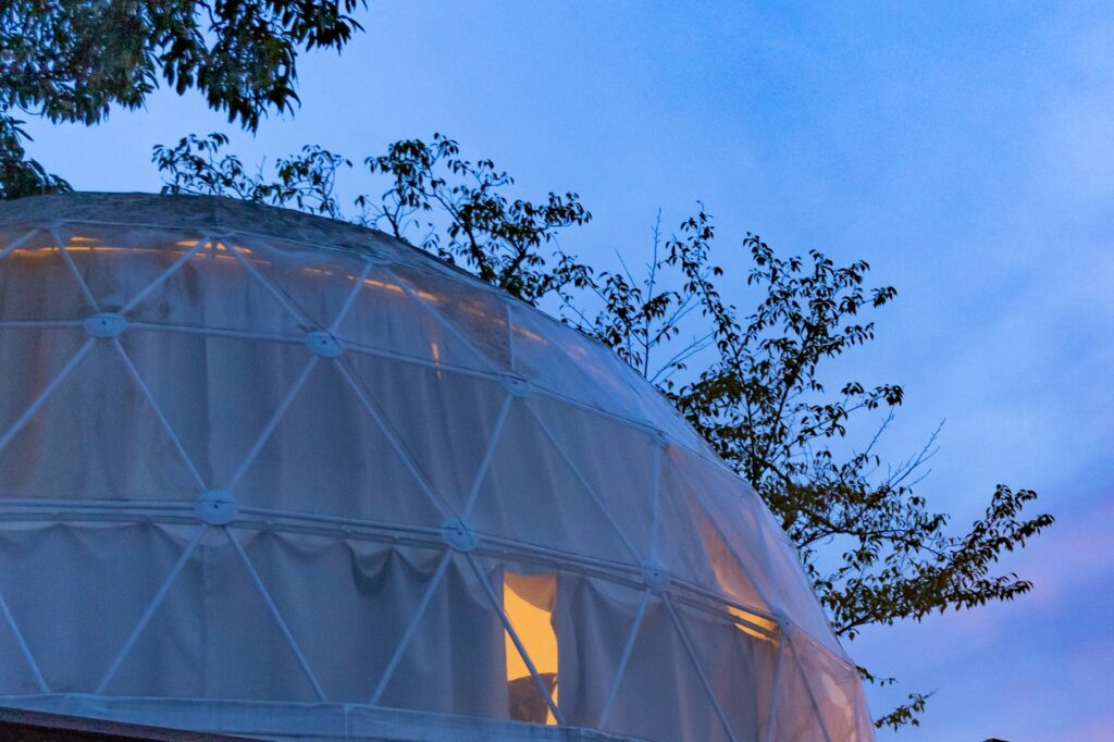 夕暮れ時に温かい光でライトアップされたおしゃれなドーム型テントの外観
