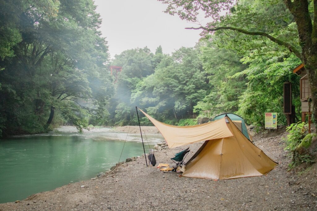川沿いのキャンプ場でワンポールテントとタープを連結して設営したソロキャンプの風景