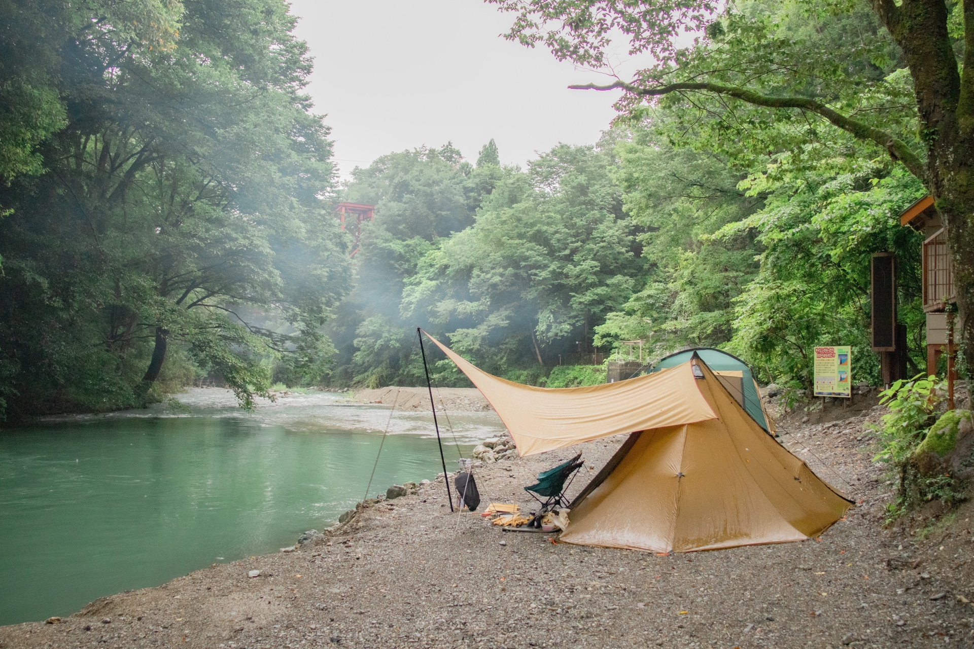川沿いのキャンプ場でワンポールテントとタープを連結して設営したソロキャンプの風景