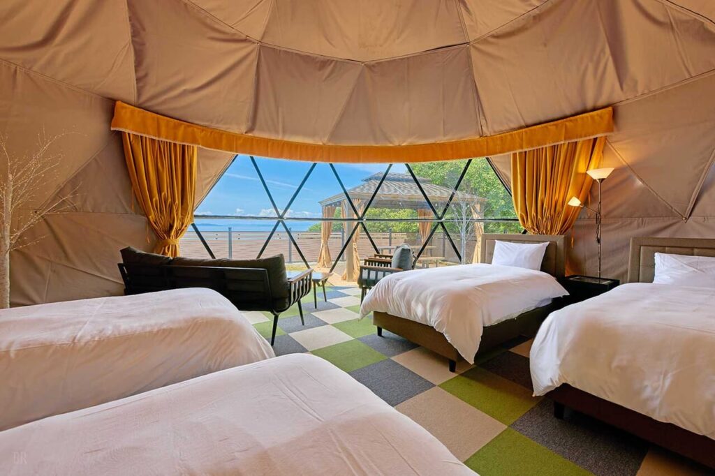海を望む大きな窓とベッド4台を備えた広々としたドームテントのラグジュアリーな室内
