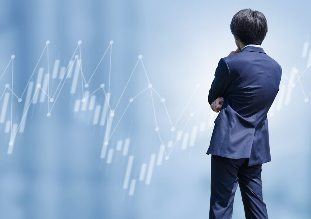 株価チャートの背景と、市場動向を分析・思案しているスーツ姿の男性