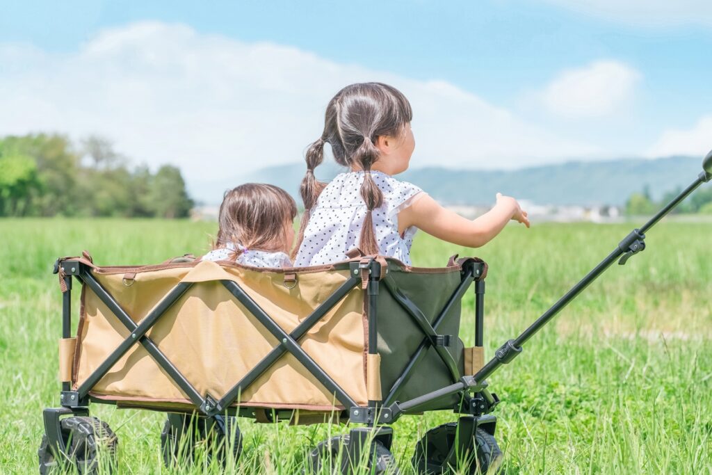 緑の野原でアウトドアワゴンに乗り、遠くの景色を指さしている二人の女の子