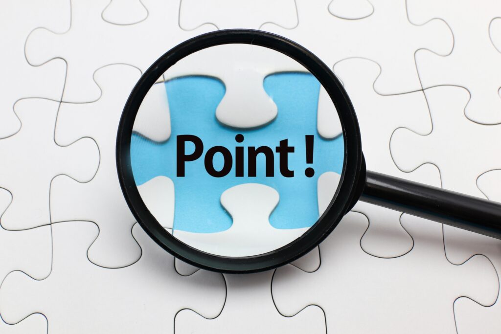 「Point!」という文字の書かれた青い背景を拡大して見せている、白いジグソーパズルの上に置かれたルーペ