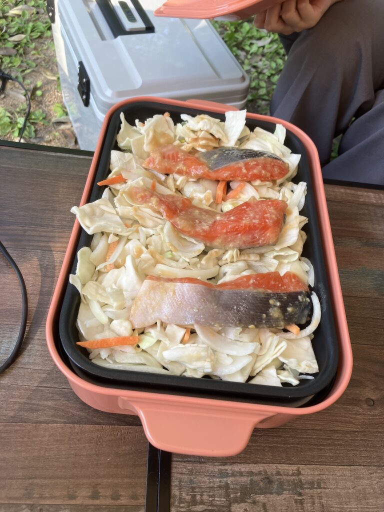 ホットプレートに敷き詰められたカット野菜の上に、下味のついた鮭の切り身が3切れ並んでいる様子。